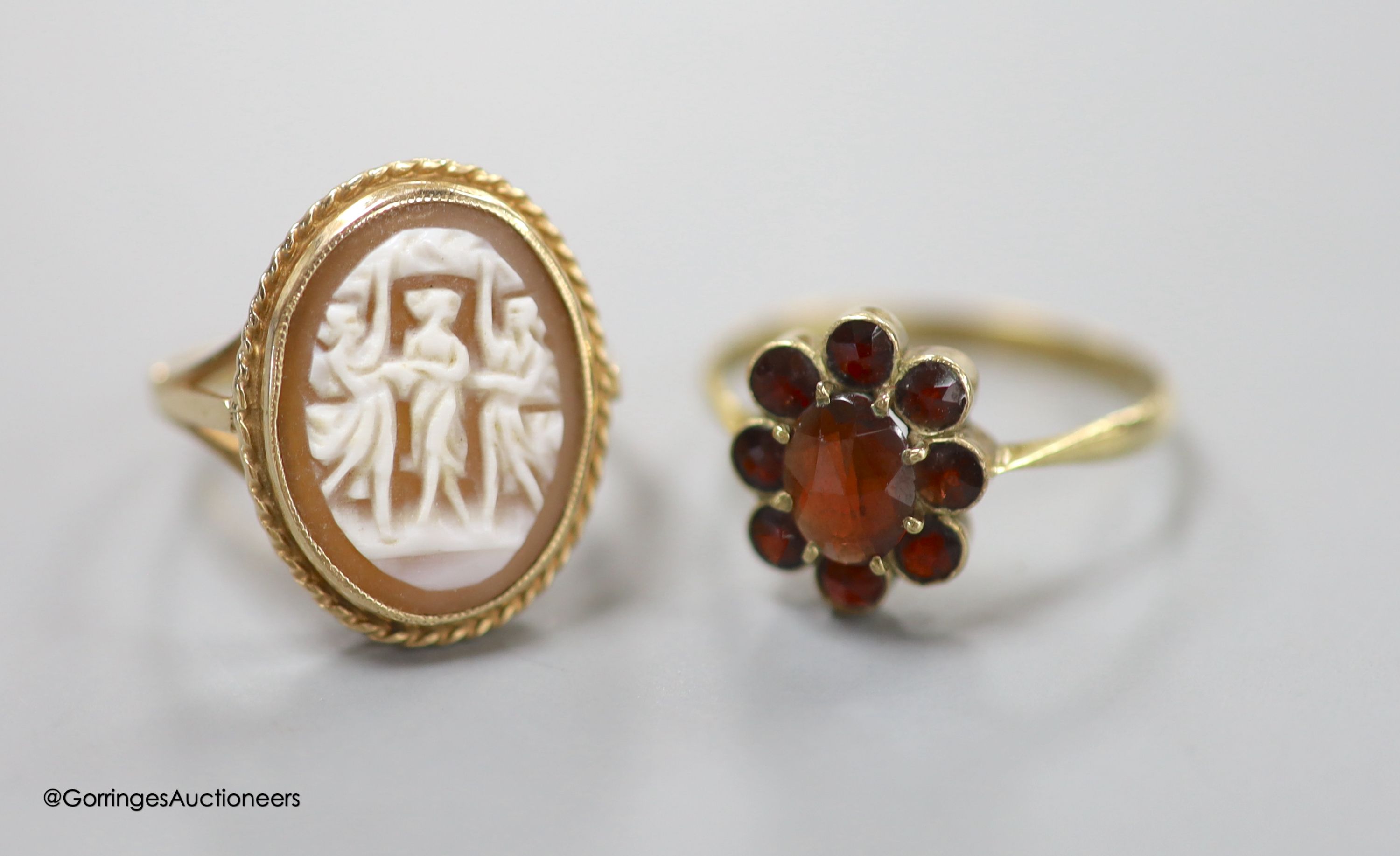 A modern 9ct gold and 'Three Graces' oval cameo shell ring, size K, gross 3.2 grams and a 333 (8kt) yellow metal and garnet cluster ring, size O/P, gross 1.7 grams.